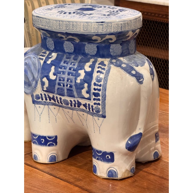 A blue and white ceramic elephant stool with a flat oval seat and four molded legs. The body is decorated with painted...