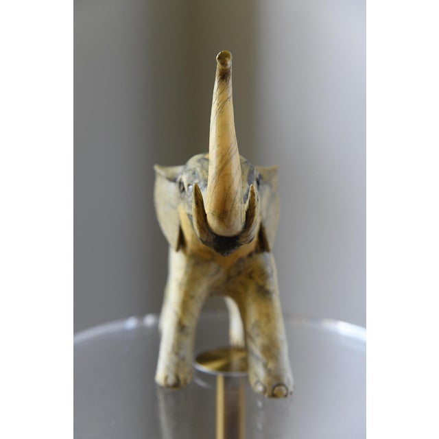 Vintage elephant sculpture featuring a raised trunk and a beautifully aged ivory/cream, grey and dark toned surface with...
