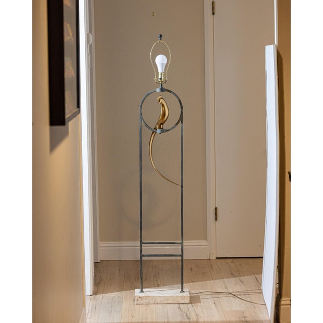 A striking sculptural floor lamp blending architectural steel, polished brass, and solid travertine into a highly refined...
