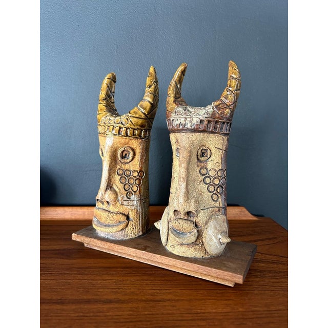 Whimsical pair of ceramic viking faces on a wood base created by artist Hal Fromhold. Art piece includes a hand-written...