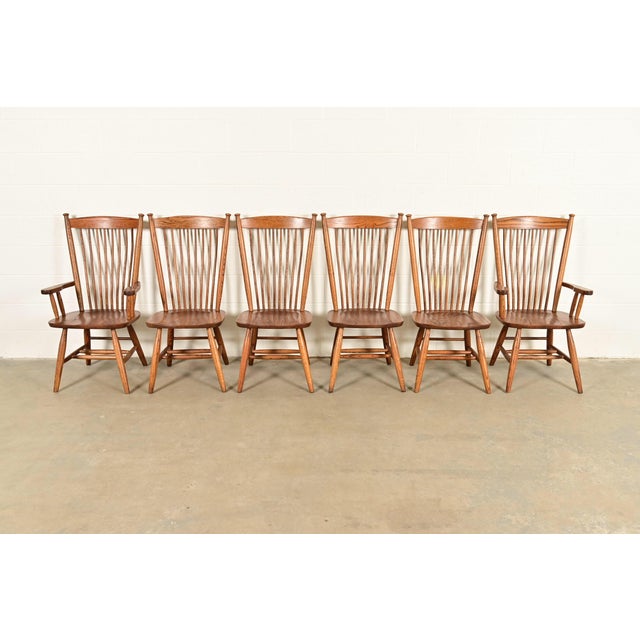 A gorgeous set of six American Colonial or Arts & Crafts style solid oak spindle back Windsor dining chairs In the manner...