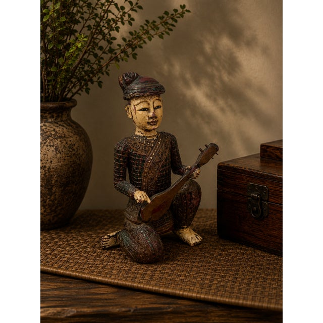 This expressive hand-carved Chinese wooden figural sculpture depicts a seated musician holding a stringed instrument,...