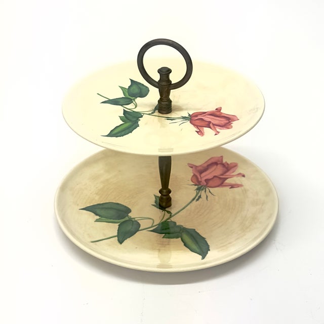 White floral ceramic cake stand. This mid-century piece is a white ceramic cake stand with two tiers, featuring a rose...