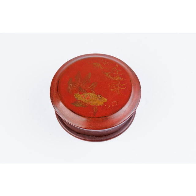 A charming antique Chinese red lacquer box of circular form, the lid finely hand-decorated in gold with a goldfish among...