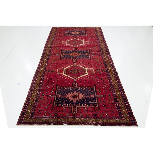 This vintage Persian Heriz rug is made of hand-knotted wool. The red field features a captivating tribal pattern in shades...