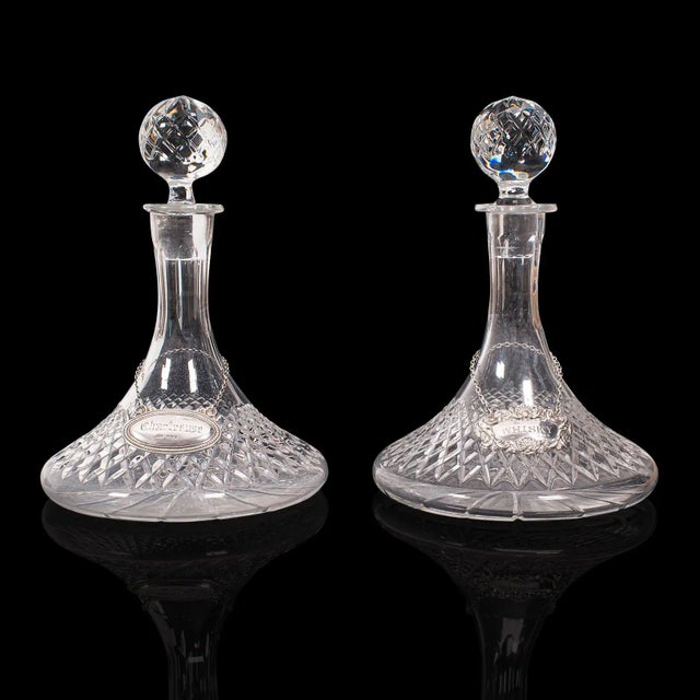 This is a pair of vintage decanters. An English, cut glass spirit vessel with hallmarked silver labels, dating to the mid...