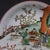 This finely hand-painted porcelain plate features a vibrant figural scene rendered in the wucai palette, combining...