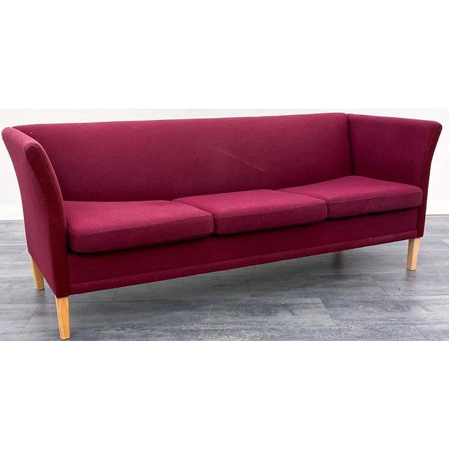 A Danish modern sofa upholstered in a classic deep red fabric. The sofa is a simply designed 3 seat flared back sofa with...