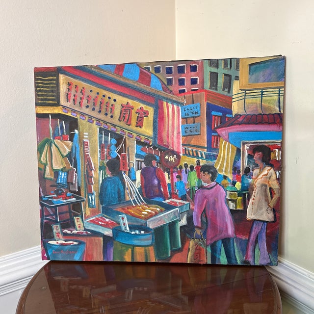 The painting depicts a bustling city street filled with people shopping at an outdoor market. The scene is vibrant and...