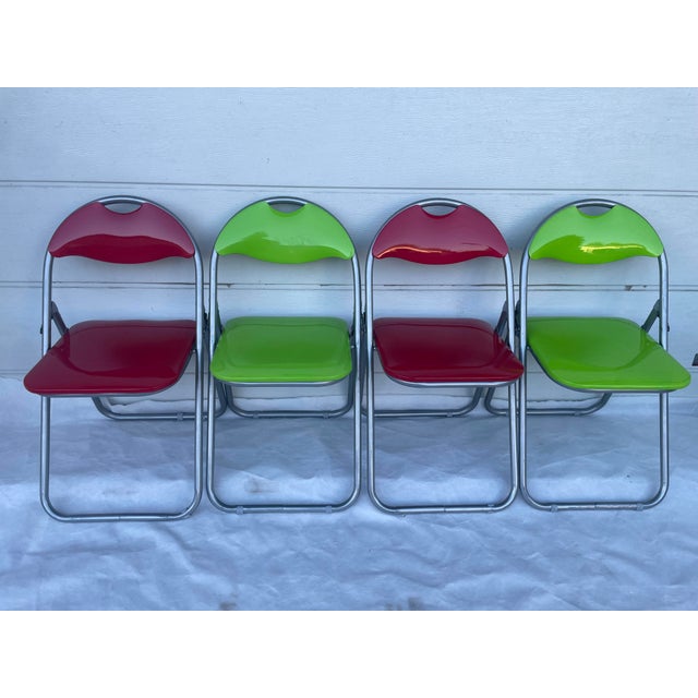 A set of 4 designer folding chairs in a striking red and lime green color scheme. The design evokes the modern design/pop...