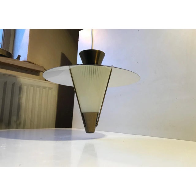 A spinning top shaped pendant lamp composed of a brass top, black lacquered aluminium shade and a brass supported conical...