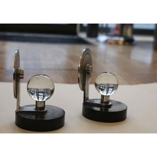 Pair of modernist paperweights functioning as bookends, made of nickel-plated metal with a black marble base and adorned...