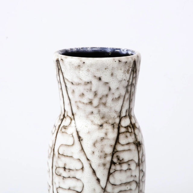 This Mid-Century Modernist White and Earth Toned Ceramic Vase With Leaf Motif is a beautiful example of Post War European...