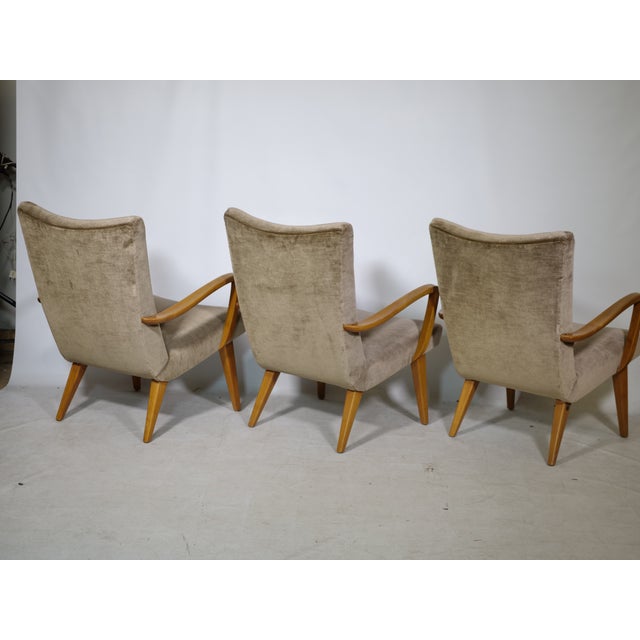 Three mid-century lounge chairs upholstered in velour from the 1960s. Curved wooden armrests and tapered wooden legs....