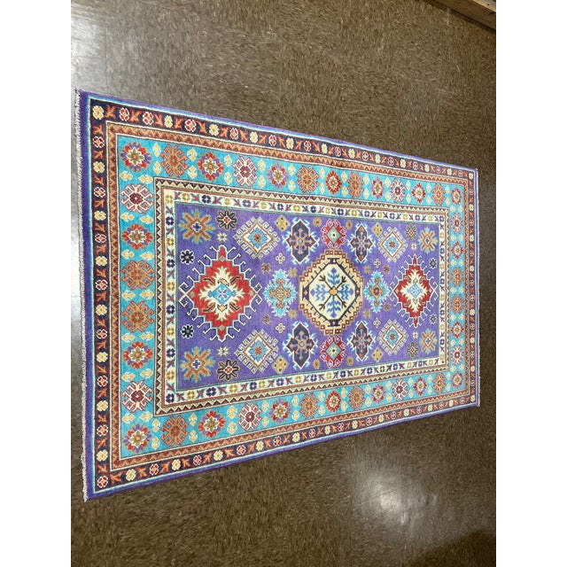 Hand-knotted Pakistani Kazak wool rug featuring a vibrant field with geometric medallions and stylized tribal motifs...