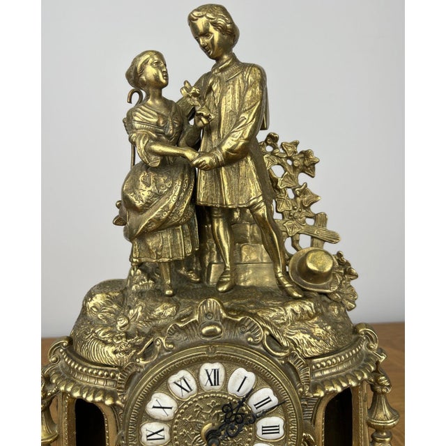 An elegant Vintage brass clock featuring an ornate figural design with a beautifully detailed romantic scene above the...