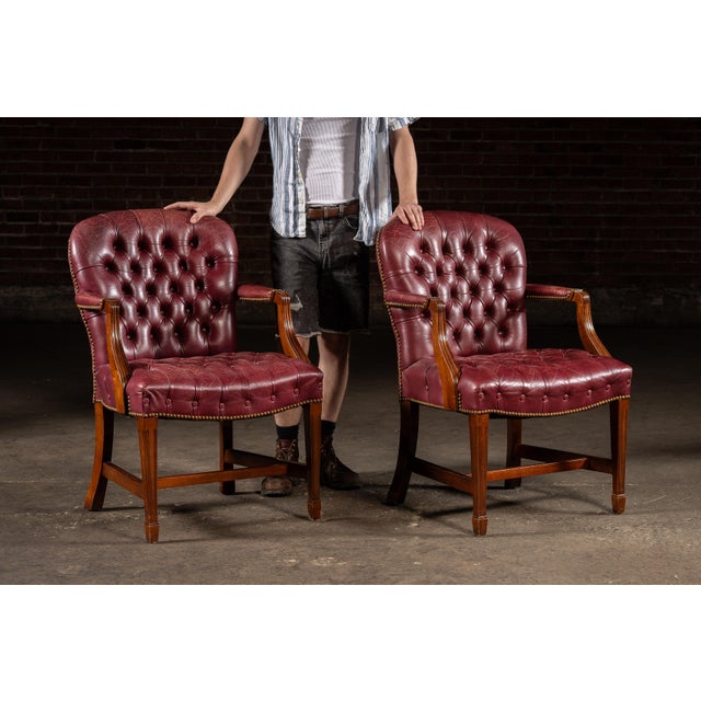 Elegant pair of round-backed dining chairs upholstered in richly toned burgundy leather with deep button tufting and brass...