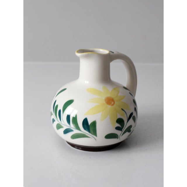 A 1950s vintage Nasco pottery pitcher with hand-painted florals in soft yellow and deep green. The rounded mid-century...
