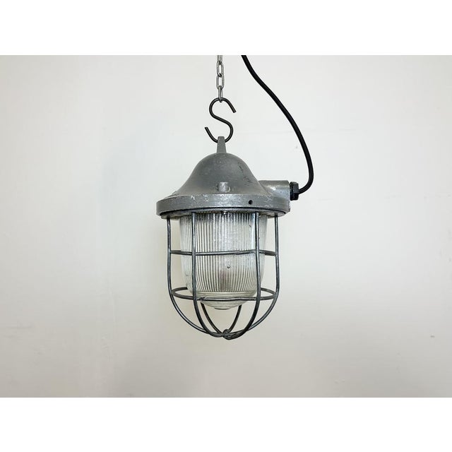 Grey industrial lamp made by Polam Gdansk in Poland during the 1960s. It features a cast aluminium body, an iron cage and...