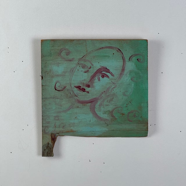 A dreamy and whimsical painting of a woman's face on a piece of wood. With a beautiful teal background and lines in...