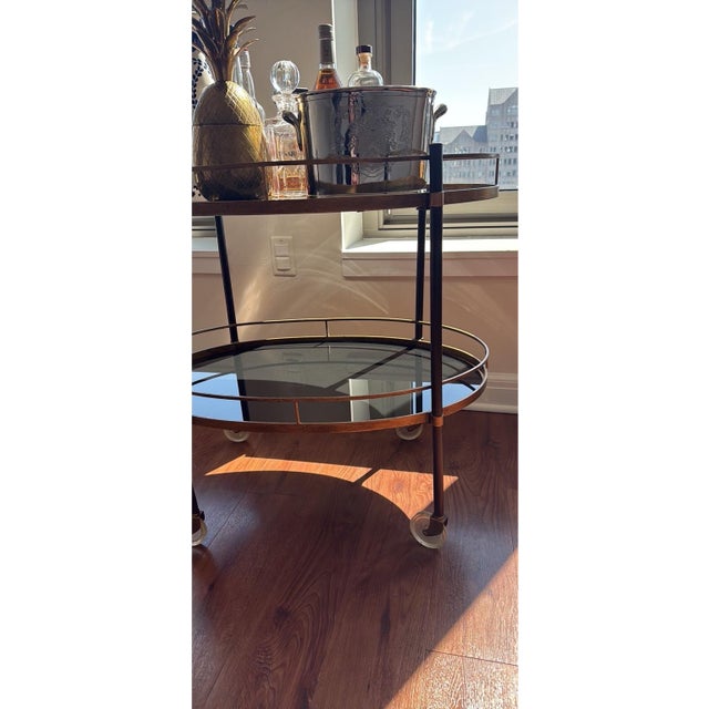 Elegant vintage bar cart featuring a warm antique brass finish with two oval glass tiers and a sleek, open frame. The...