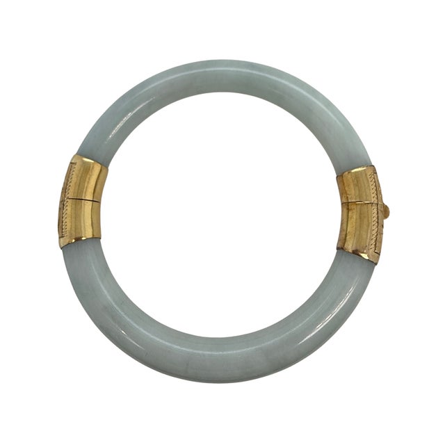 Softly mottled light green jadeite meets warm 14-karat yellow gold in this Chinese hinged bangle bracelet. The jade is cut...