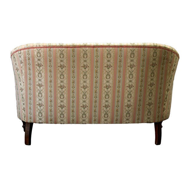 A vintage two-seater sofa with a high, enveloping back and a gently curved upper section that seamlessly merges with the...