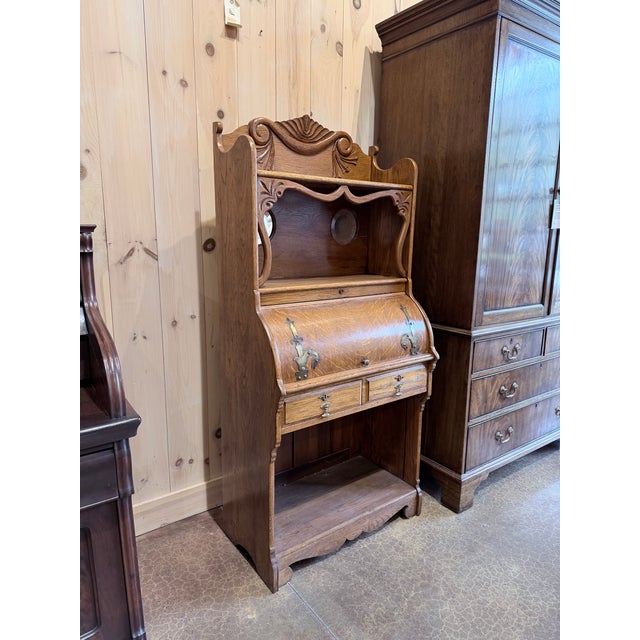 A charming early 20th century oak cylinder roll secretary desk showcasing warm oak grain, graceful curves, and decorative...