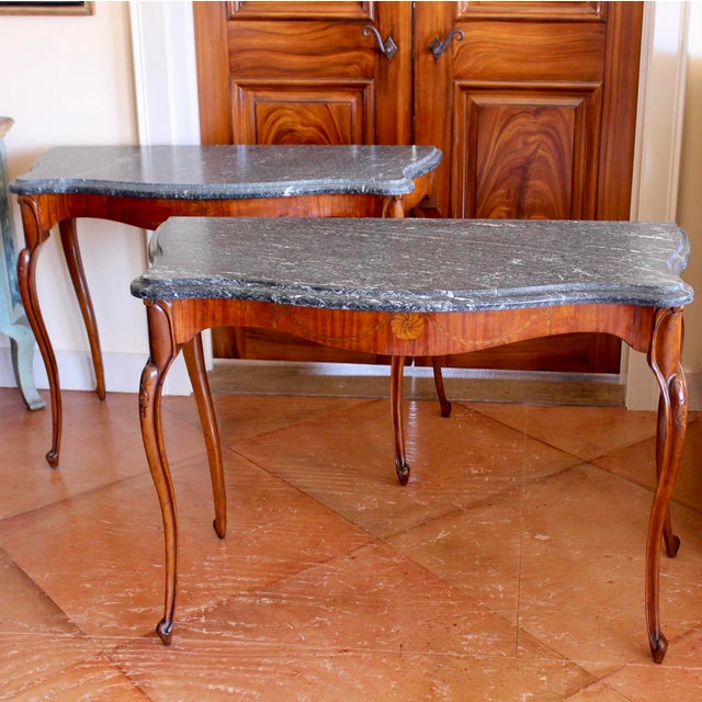 A stylish pair of slender console tables, of warm golden toned satinwood paired with chic dark gray custom marble tops....