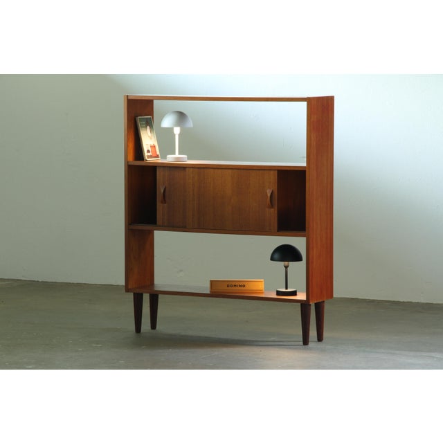 Danish bookcase in teak, produced during the 1960s. The design features two open shelves and a central cabinet with...