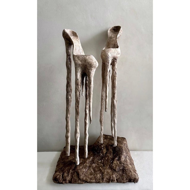 This artwork features two abstract sculptures resembling shoes, crafted from plaster and steel. The elongated forms drip...