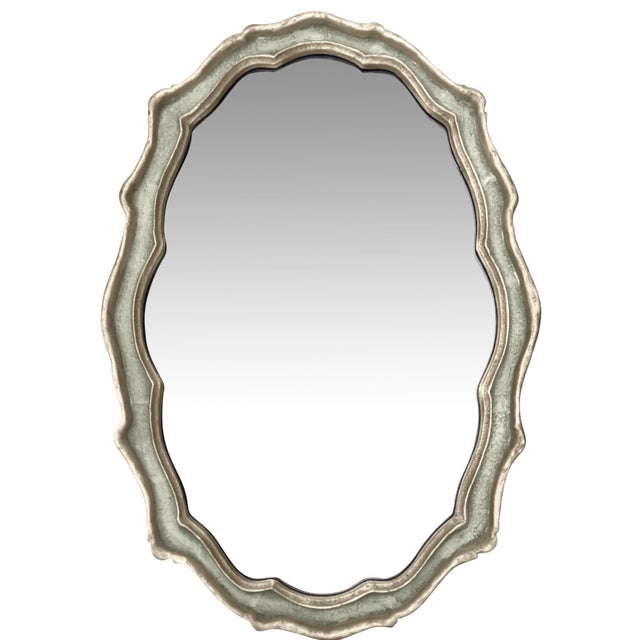 Solid cast metal oval mirror in a scalloped cartouche form. Silver-gilt finish — a warm amalgam of silver finish with a...