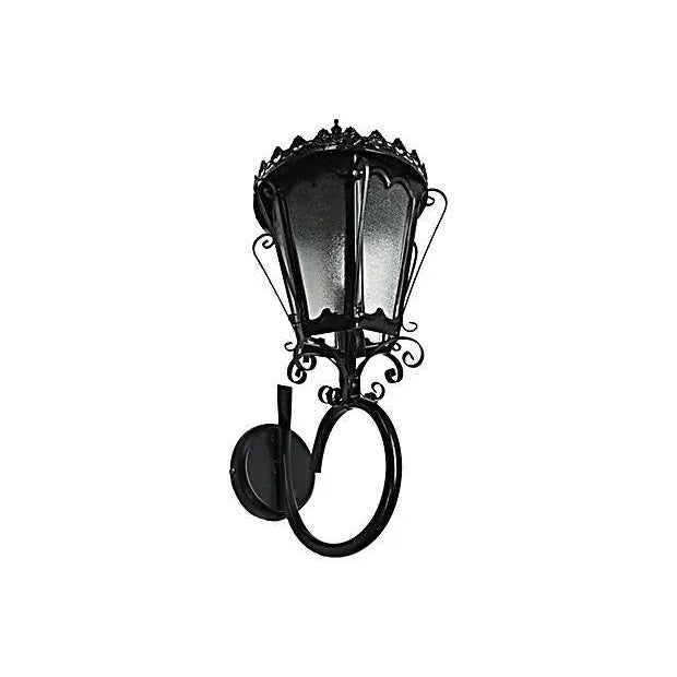 Spanish Colonial-style lantern sconce with a trapezoidal shape. The lantern has six corrugated frosted glass panes...