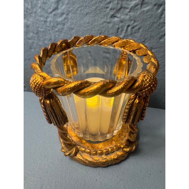 A pair of gilt metal candle holders in the neoclassical rope-and-tassel manner, each with a fluted glass votive insert....