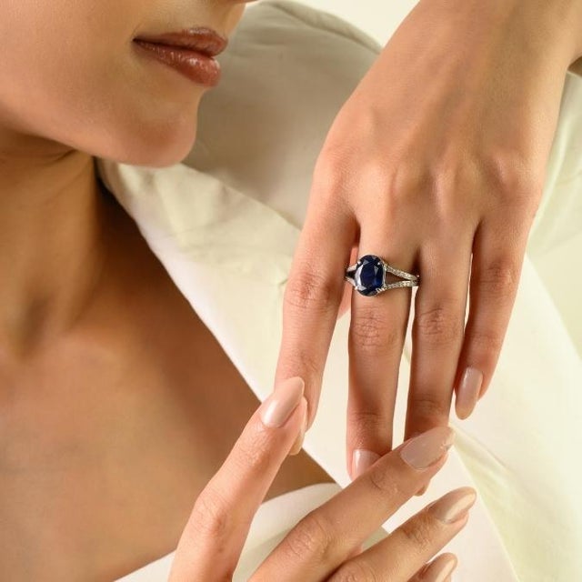 This elegant split-shank ring features 1 natural oval-cut blue sapphire totaling approximately 4.57 carats, beautifully...
