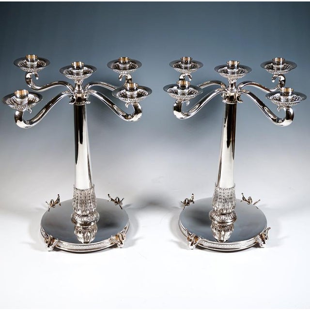 Two elegant five-flame candlesticks on a wide, round base with a flat, smooth top and a relief border on the sides,...