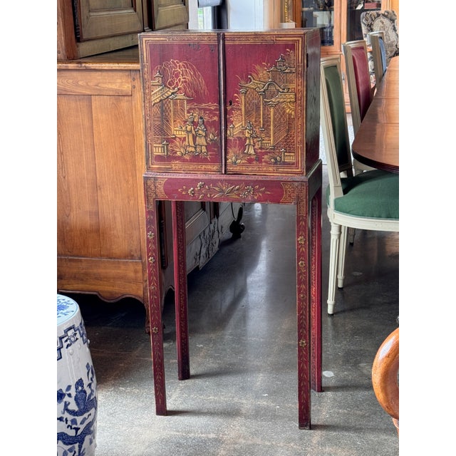 Red lacquered collector’s cabinet raised on a stand, the pair of doors decorated in raised gilt chinoiserie with figures,...