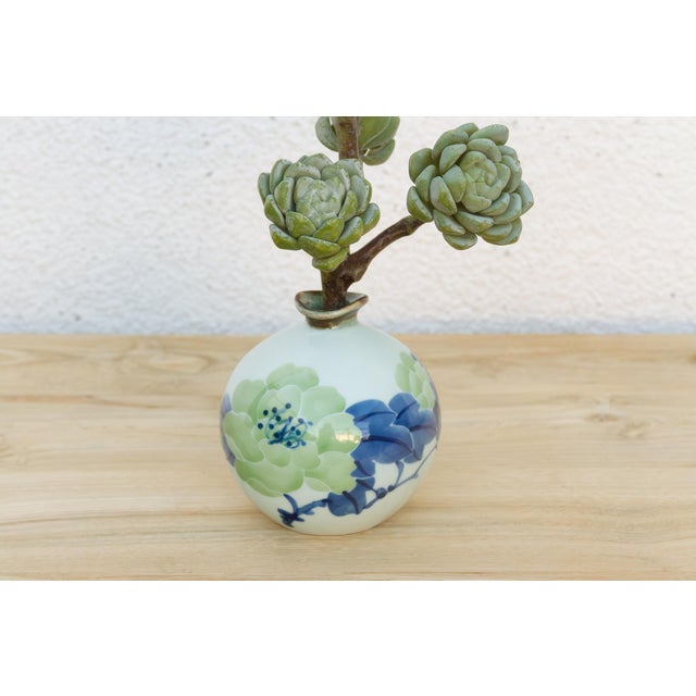 A small vintage vase with a pair of layered blossoms, one in soft green, one in deeper blue, share the body in a single...
