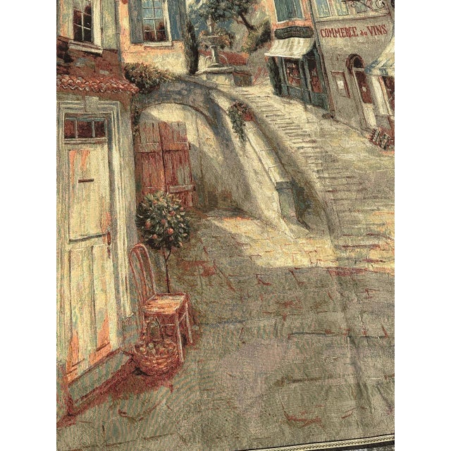 Vintage decorative tapestry featuring a charming European village street scene. The artwork depicts narrow cobblestone...