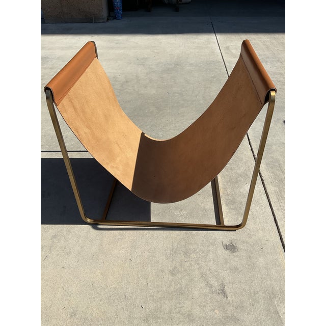 Elevate your living space with this sculptural contemporary magazine rack featuring a rich cognac saddle leather sling...