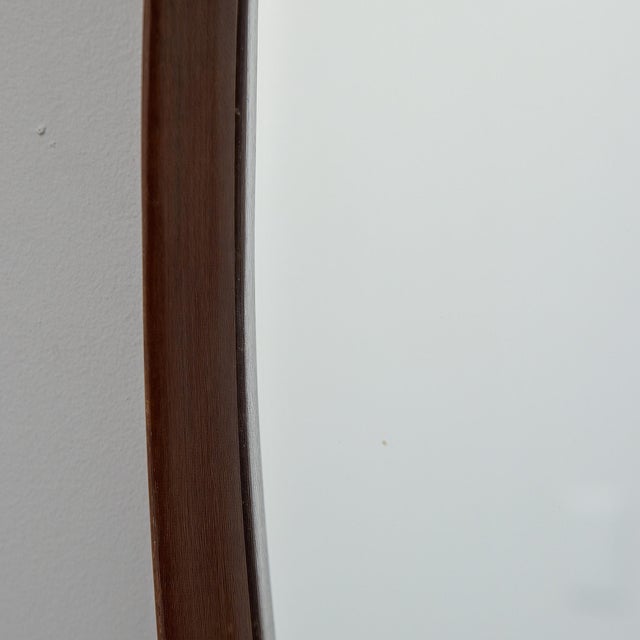 Elongated oval mirror set within a deeply contoured walnut frame. The rounded profile gives substantial depth, casting...
