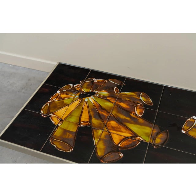 Rectangular coffee table with chrome structure and square tile top with a black background and tubular colored motifs.
