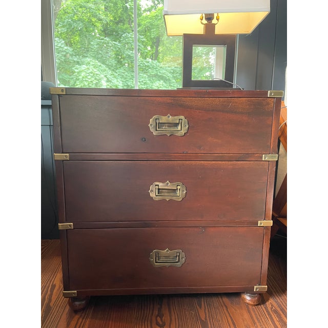Pair of vintage campaign-style bedside chests / end table / dresser in mahogany-toned hardwood. Each features three...