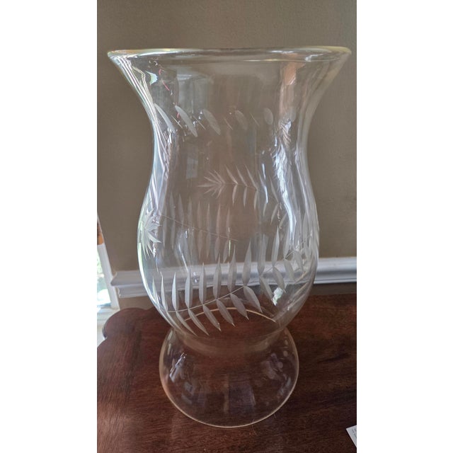 Single round clear glass candle hurricane shade with curved sides with etched fern design. The fern etching begins at the...