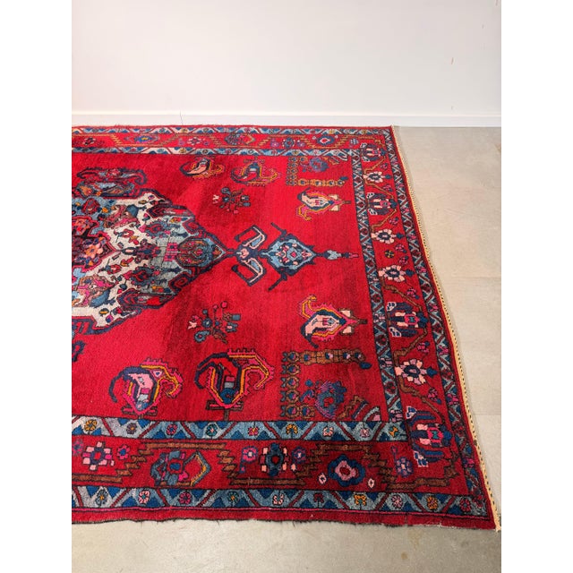 A striking vintage hand-knotted Bakhtiar rug from Iran, featuring a vibrant ruby red field contrasted with deep blues,...