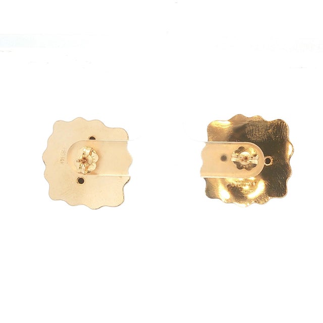 A pair of 14k gold stud earrings featuring red garnet cabochons. The design includes a wavy gold border. In good condition.
