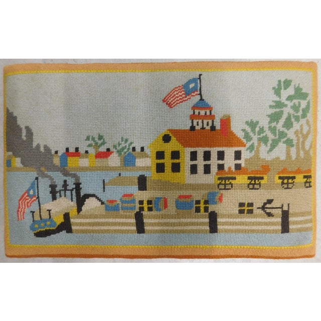 Solid wood stool with hand-woven folk-art needlepoint depicting a steamboat and houses in the background.