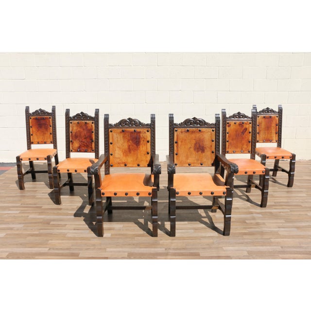 Beautiful vintage set of six Spanish Revival dining chairs featuring dark carved wood frames paired with warm tan leather...