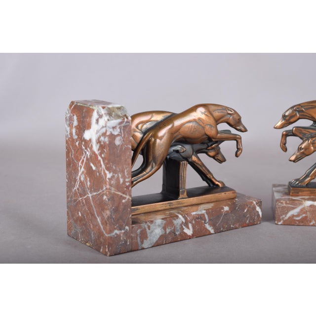 Pair of Art Deco bookends, dated to the 1930s. Each L-shaped red marble base with white veining carries two running...