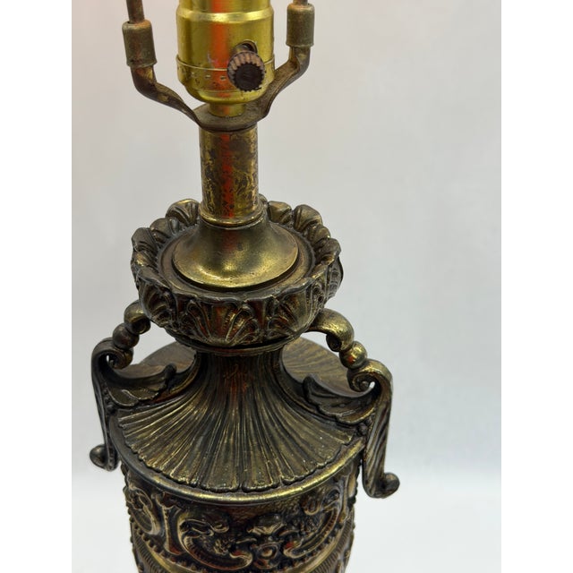 Vintage Neoclassical urn-style table lamp featuring an ornate cast metal body with relief scrollwork, acanthus leaf...